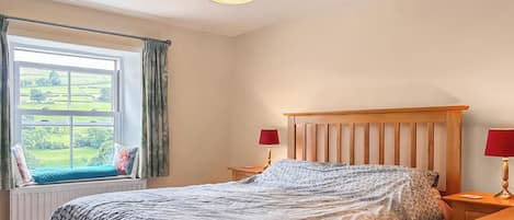 A bedroom with a bed, two bedside tables, a window with curtains, and a hanging lamp.