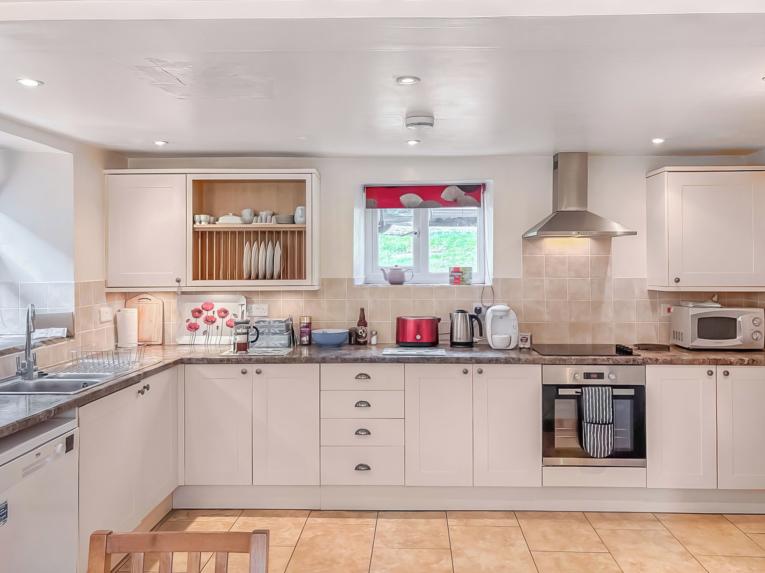 A modern kitchen with white cabinets, a window with red curtains, and a stainless steel range hood.