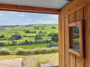 Ein Fenster mit Holzrahmen und Blick auf sanfte, grüne Hügel und einen klaren Himmel.