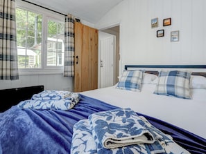 Um quarto com uma cama, porta de madeira e janela com cortinas.