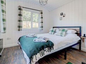 A bedroom with a bed, a window with curtains, a bedside table, and a wall-mounted light fixture. - 2 bedroom accommodation in Whitwell (Whitwell)