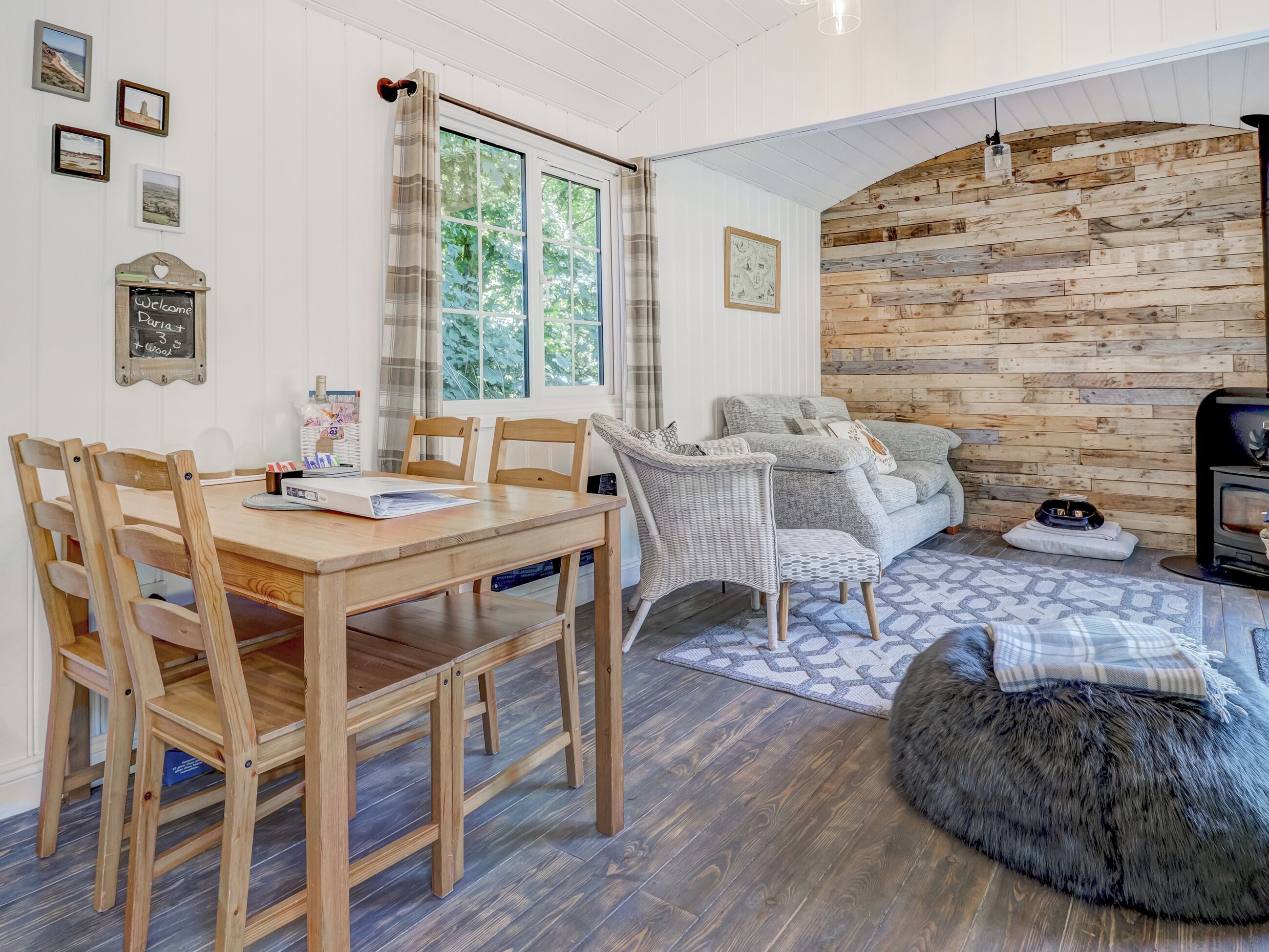 A cozy living area with a wooden dining table, wicker chairs, a grey sofa, and a fireplace.
