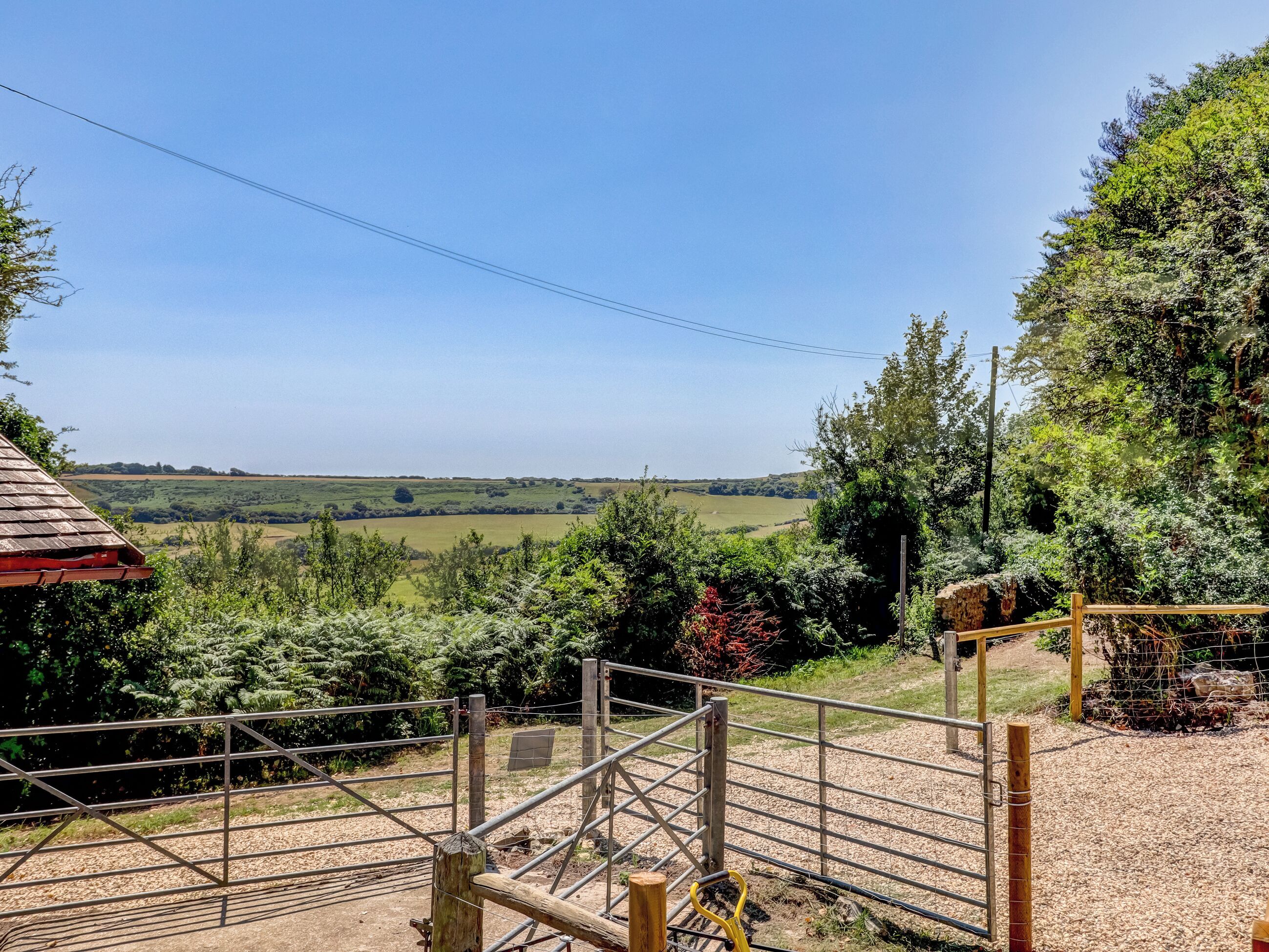 A rural landscape with a metal gate, wooden fence, and a view of open fields.