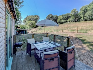An outdoor deck with a glass-top table and wicker chairs, surrounded by a wooden deck and a view of a grassy field. - 2 bedroom accommodation in Whitwell (Whitwell)