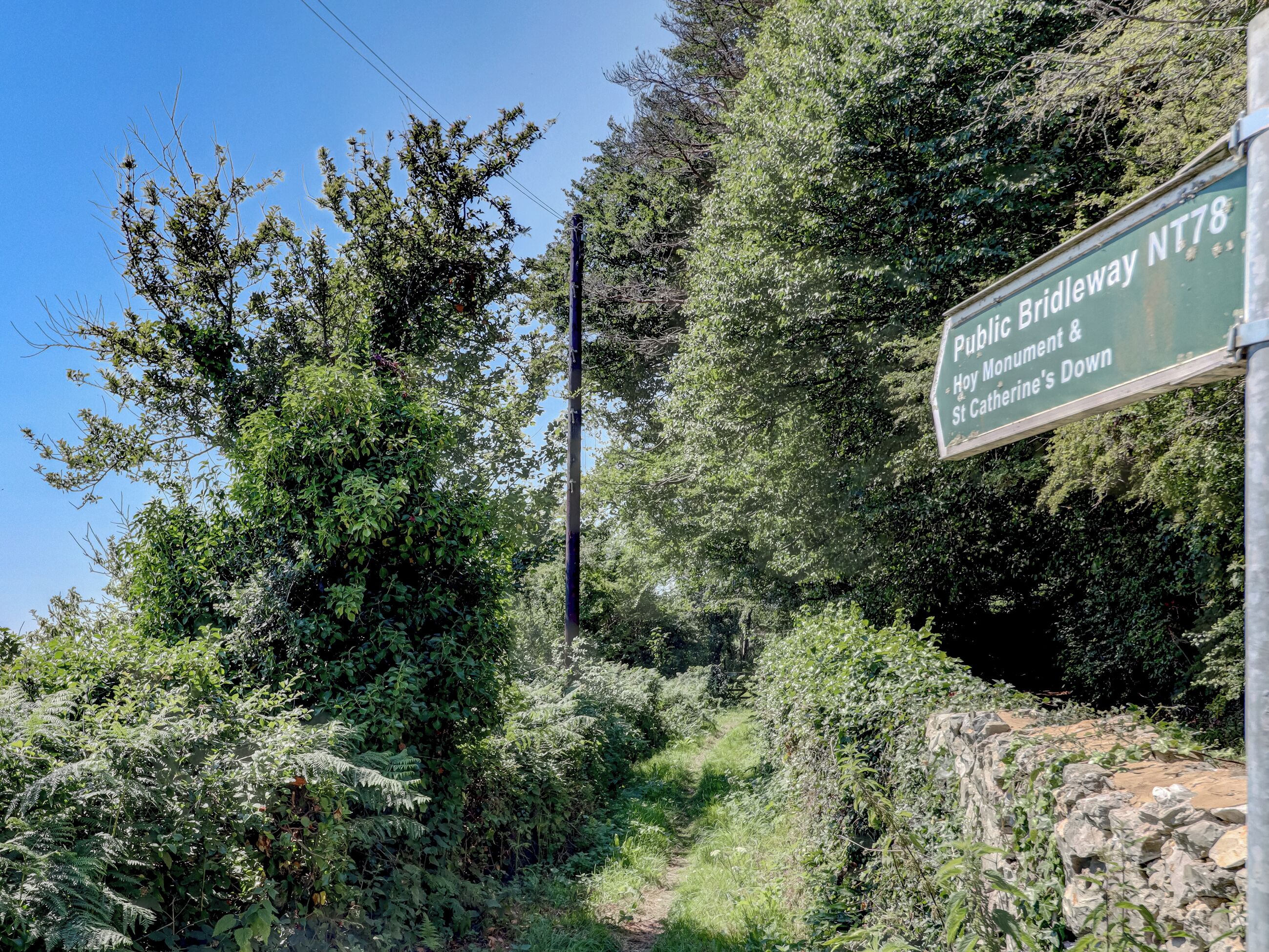 Un panneau indiquant un sentier public pour cavaliers, NT78, St Catherine's Down, avec un paysage naturel en arrière-plan.