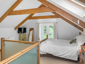 A bedroom with a sloped ceiling, a bed, a dresser, a television, and a window with curtains. - 2 bedroom accommodation in Holsworthy (Holsworthy)