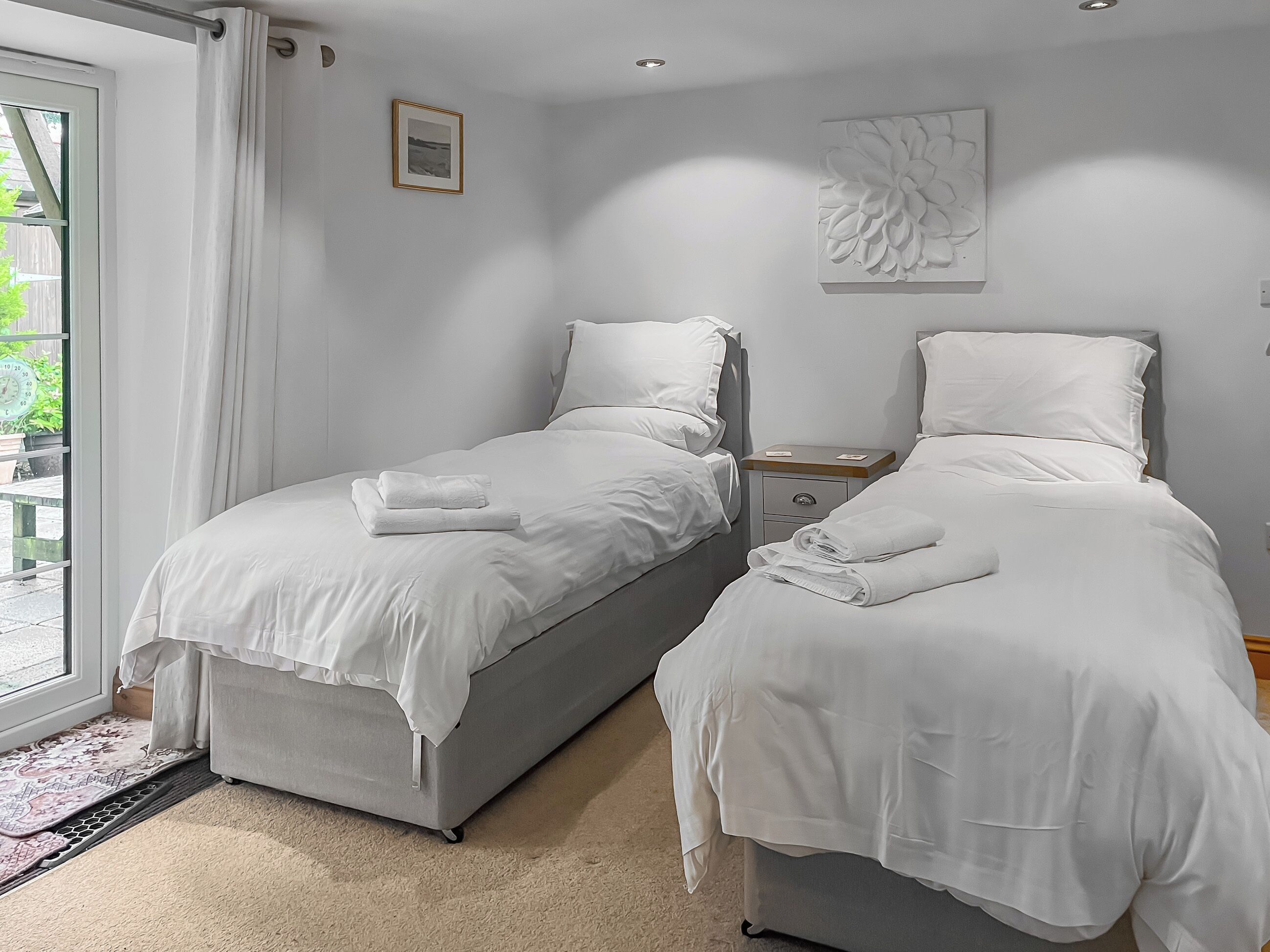 Een slaapkamer met twee bedden, een klein nachtkastje, een raam met gordijnen en een aan de muur hangend schilderij.