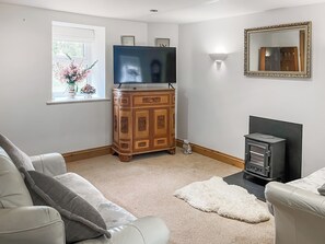 A living room with a television, wooden cabinet, fireplace, and a sofa. - 2 bedroom accommodation in Holsworthy (Holsworthy)