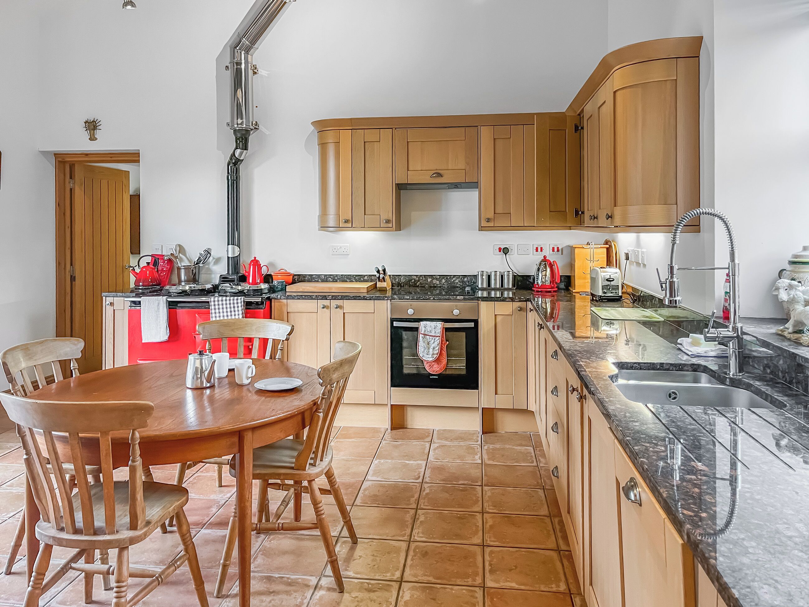A kitchen with wooden cabinets, a red stove, a dining table with chairs, and a tiled floor.