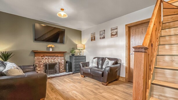 Ein Wohnzimmer mit Kamin, einer Couch, einer Holztreppe und einem an der Wand befestigten Flachbildfernseher.