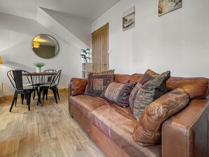 Una sala de estar con un sofá de cuero marrón, una mesa de comedor con sillas, un espejo redondo y una puerta de madera.