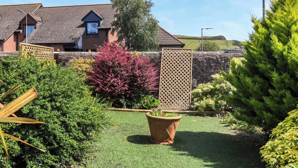 A residential property with a well-maintained lawn, a wooden fence, and a house with a sloped roof. - 1 bedroom accommodation in Banchory (Banchory)
