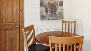 A wooden dining table with two chairs, a wooden door, and a wall-mounted picture of a yak. - 1 bedroom accommodation in Banchory (Banchory)