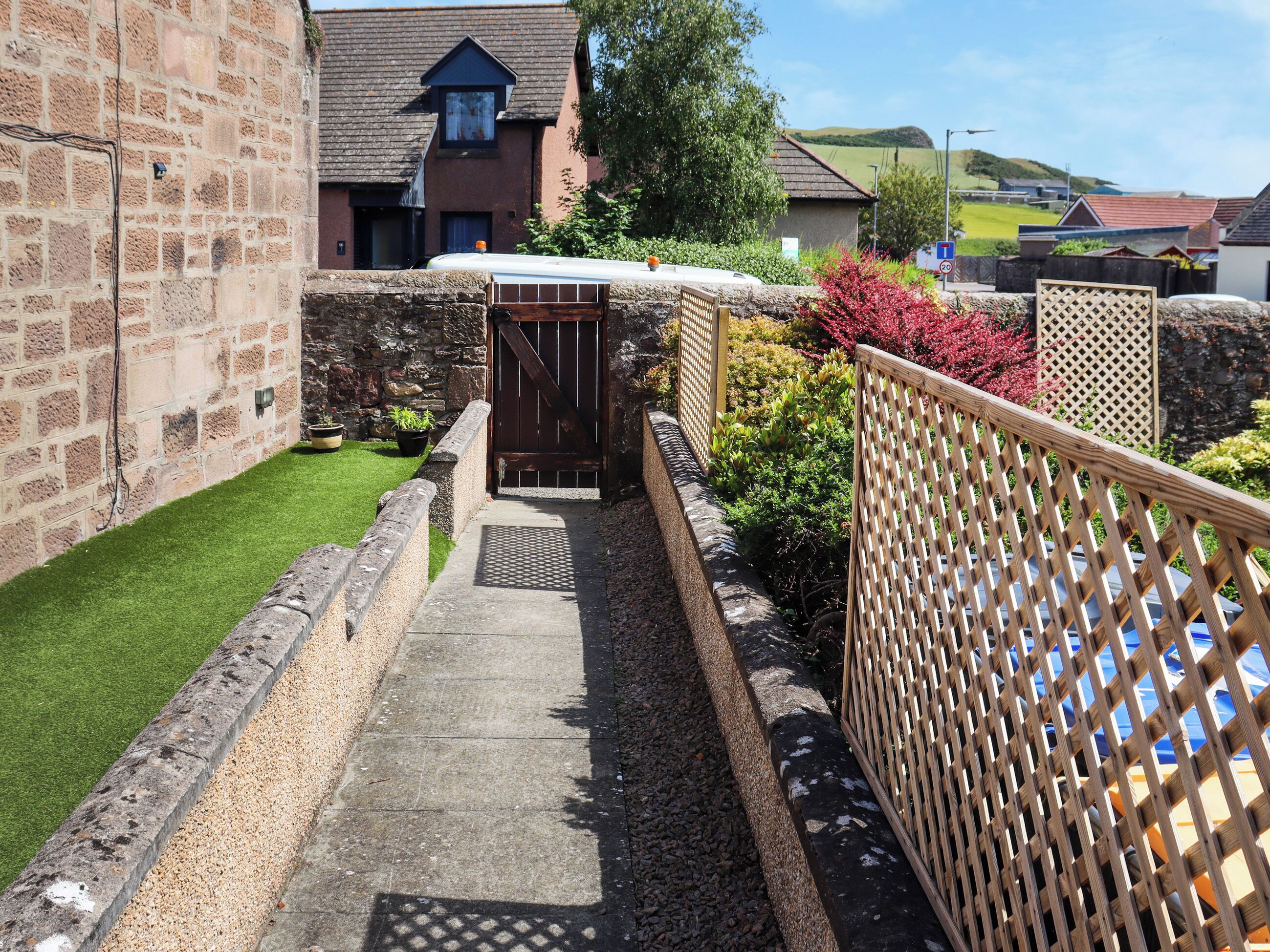 A narrow pathway leading to a gated entrance, flanked by stone walls and a wooden fence.