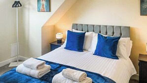 Una habitación de hotel con una cama, almohadas, una mesita de noche, una lámpara y un cuadro en la pared.