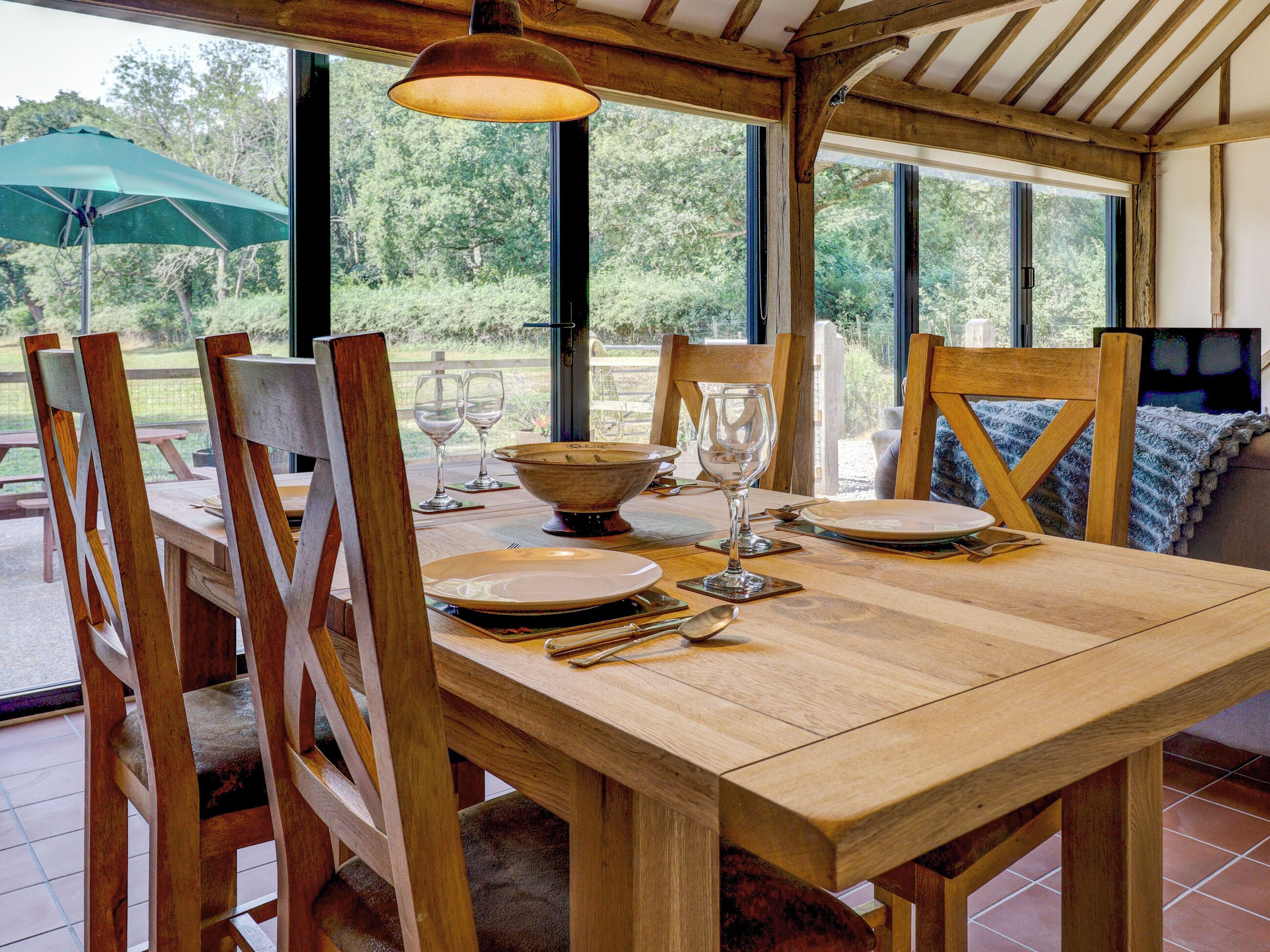Une table à manger en bois, dressée avec des assiettes, des verres et des couverts, entourée de chaises en bois, et offrant une vue sur la verdure environnante.