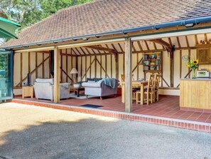A covered outdoor seating area with a wooden table and chairs, a sofa, and a bookshelf. - 2 bedroom accommodation in Steyning (Steyning)