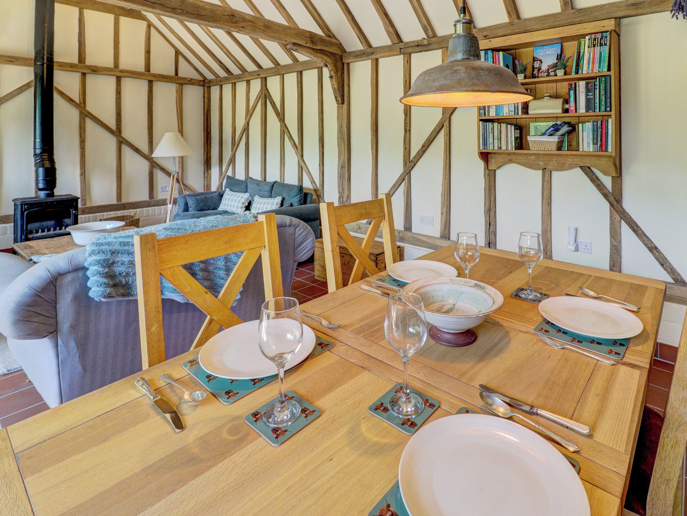 A dining area with a wooden table set for four, a bookshelf in the background, and a cozy living space with a sofa and a fireplace.
