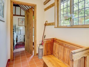 A wooden bench in a hallway with a tiled floor, a window with a view of trees, and a door leading to another room. - 2 bedroom accommodation in Steyning (Steyning)
