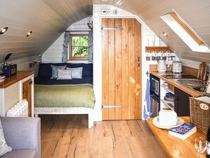 Ein gemütliches Schlafzimmer mit einem Bett, einem Fenster mit Vorhängen, einer Holztür und einer Küchenzeile mit Spüle und einer Torte auf der Arbeitsfläche.
