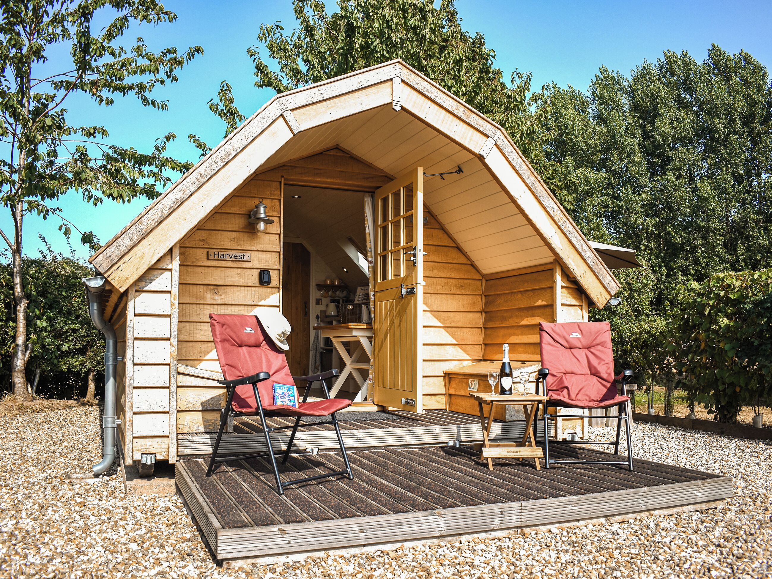 A wooden cabin with a porch, two red chairs, a table, and a bottle of wine.