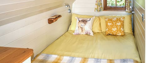 Un dormitorio con cama, almohadas, una ventana con cortinas y un estante de madera.
