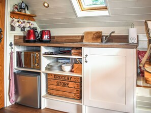 Eine kleine Küche mit Backofen, Kaffeemaschine und einem Holzregal über der Spüle.