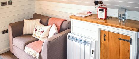 Un espacio de sala acogedor con sofá, un radiador, un armario de madera y una radio montada en la pared.