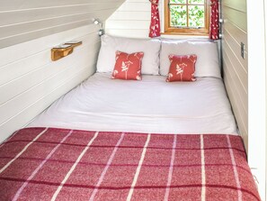 Un lit simple avec une couverture à carreaux rouges et blancs, deux oreillers à motifs floraux et une table de chevet en bois.