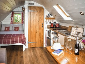 Ein gemütliches Schlafzimmer im Dachgeschoss mit einem Bett, einer Holztür und einer Küchenzeile mit Herd, Spüle und einer Weinflasche.