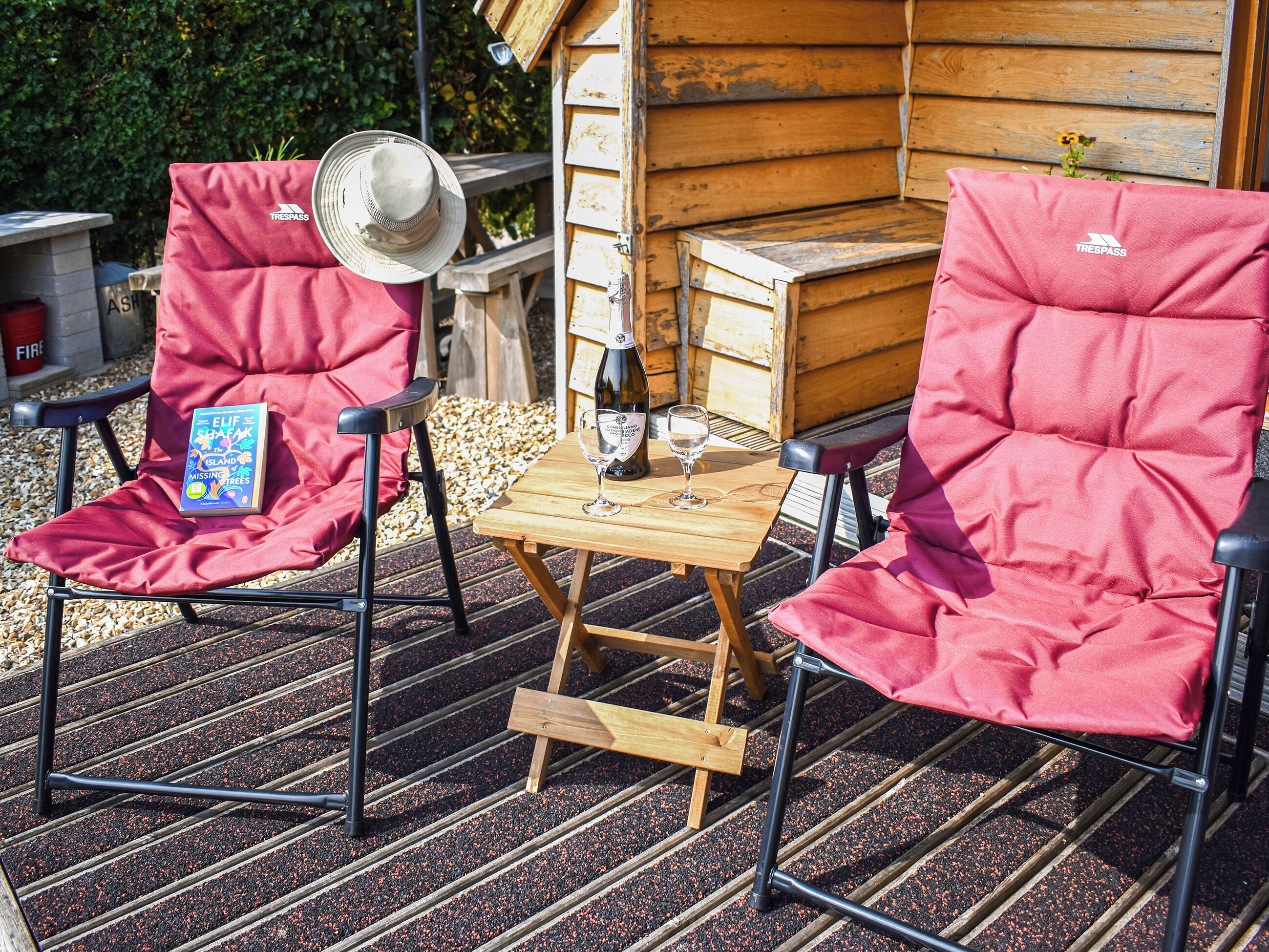 Twee rode stoelen met kussens, een klein houten tafeltje met een wijnglas en fles, en een boek op een van de stoelen.