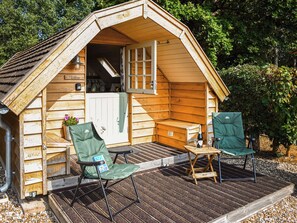 A wooden cabin with a porch, two chairs, a table, and a bottle of wine. - 1 bedroom accommodation in Sidmouth (Sidmouth)
