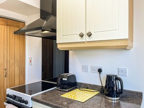 A kitchen with a stove, toaster, and kettle, wooden cabinets, and a white door. - The sea views from this property are amazing and the beach is right out front. (Hornsea)