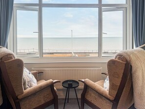 Ein Zimmer mit zwei Sesseln, die zu einem Meerblickfenster blicken, einem kleinen Tisch und einer Heizung.