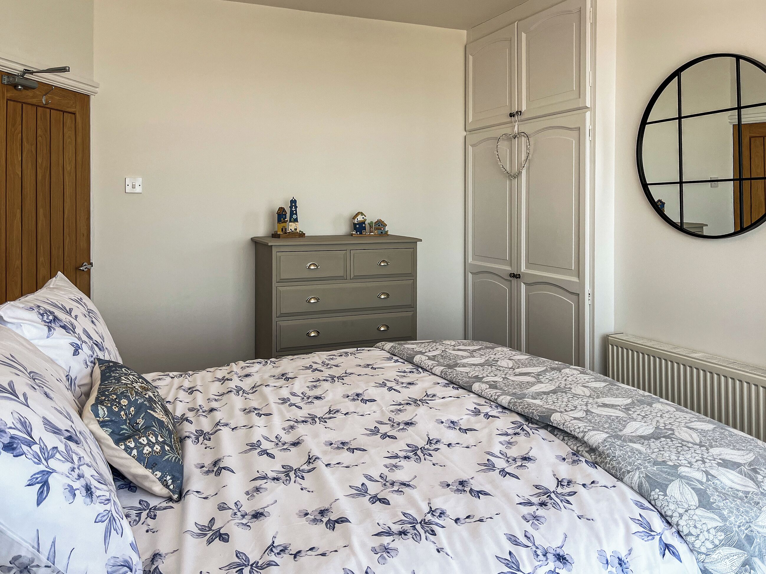 A bedroom with a bed, dresser, wardrobe, and a round mirror.