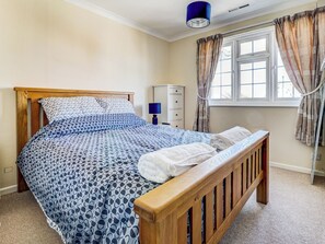 A bedroom with a wooden bed, patterned bedding, a bedside lamp, a wardrobe, and a window with curtains. - 3 bedroom accommodation in Shanklin (Shanklin)