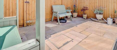 A patio with a wooden fence, a bench, potted plants, and a metal watering can.