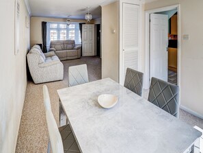 A dining area with a marble table, cushioned chairs, and a view into a living room with a sofa and curtains. - 3 bedroom accommodation in Shanklin (Shanklin)