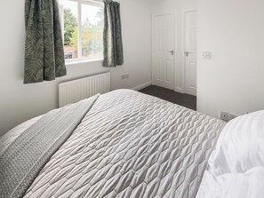Ein Schlafzimmer mit einem Bett, einem Fenster mit Vorhängen, einem Heizkörper und einer Gruppe weißer Türen.