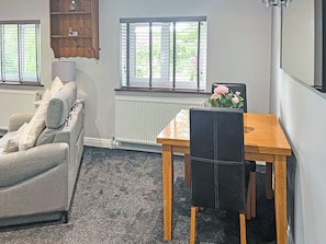 A room with a sofa, a dining table with a chair, a radiator, and a window with blinds.
