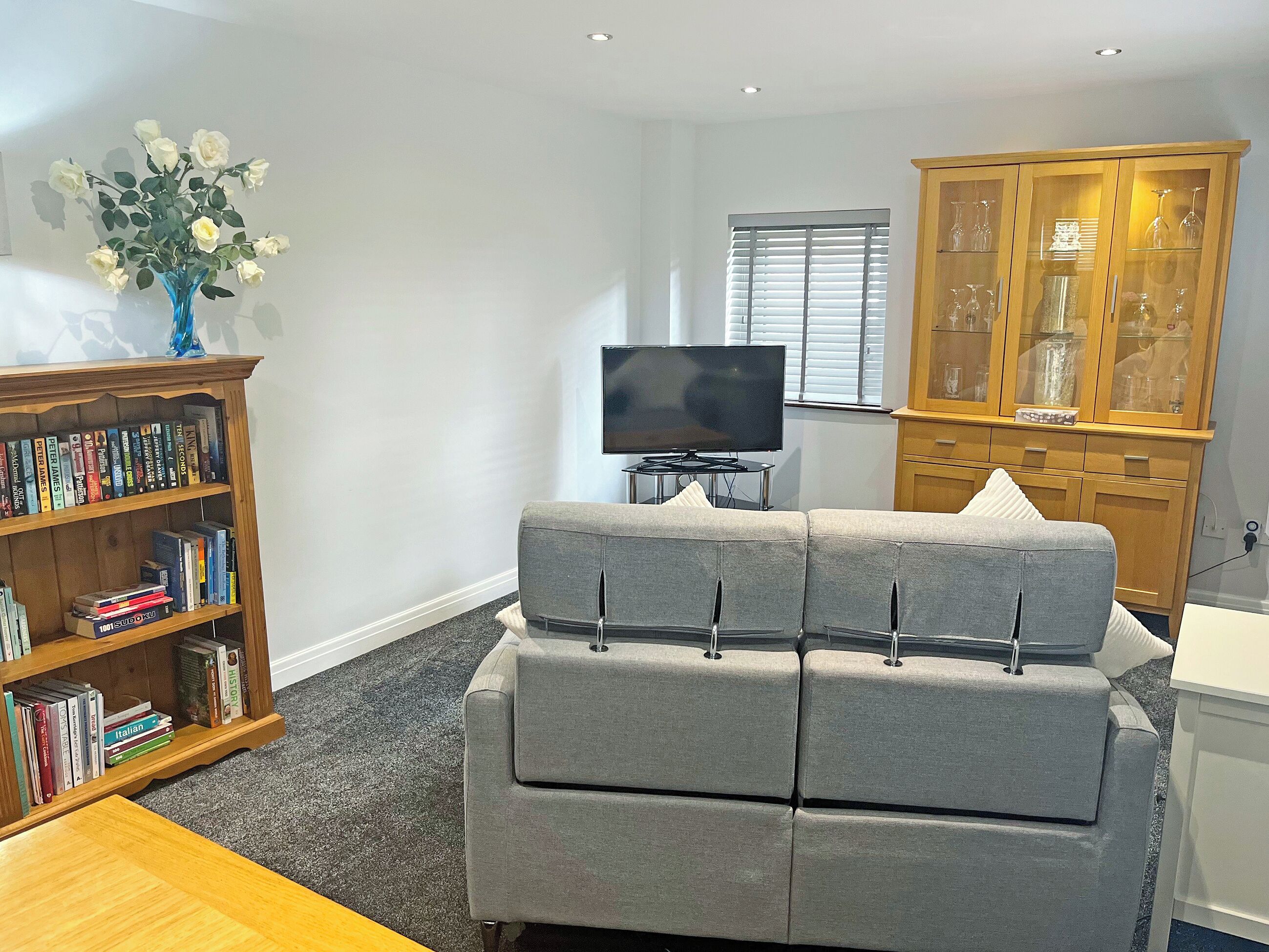 A living room with a grey sofa, a wooden bookshelf, a flat-screen TV, and a wooden cabinet with glass doors.