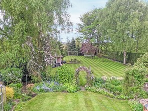 A well-maintained garden with a lawn, a wooden pergola, and various flowering plants.