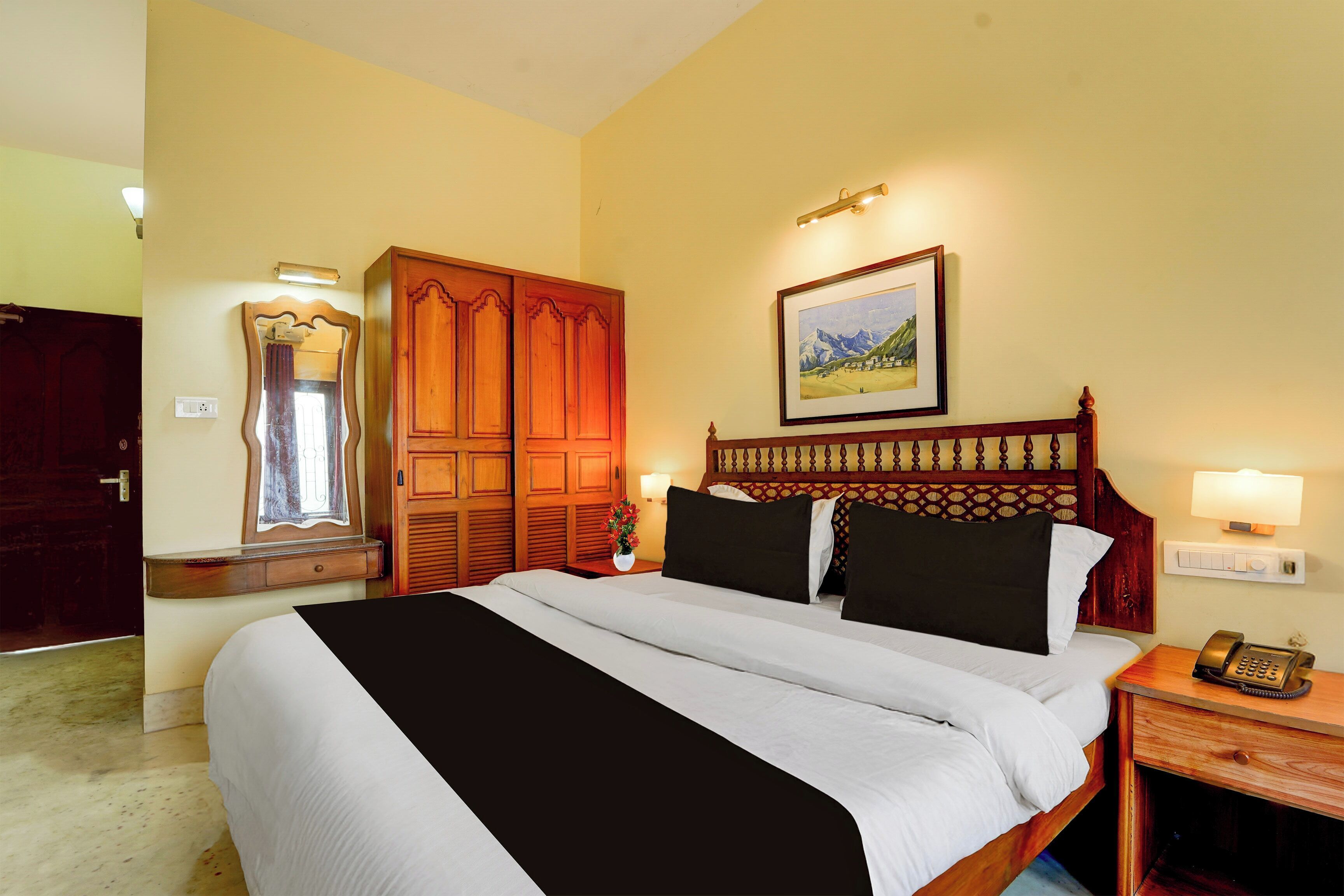 Habitación de hotel con una cama grande, armario de madera, un cuadro en la pared y una mesita de noche con lámpara y teléfono.
