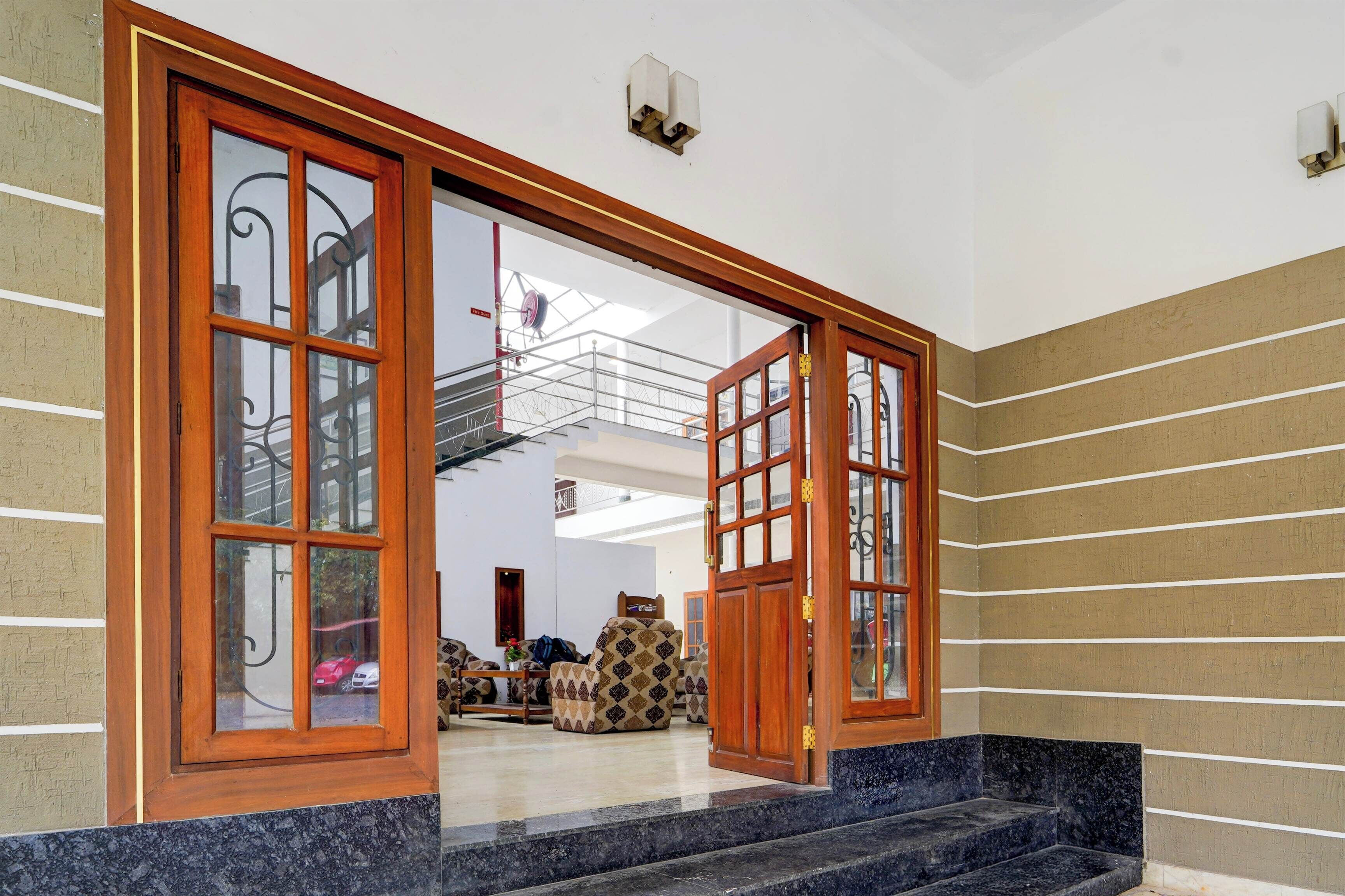 Entrada de hotel con puerta doble de madera, detector de incendios y escalera que sube al piso superior.