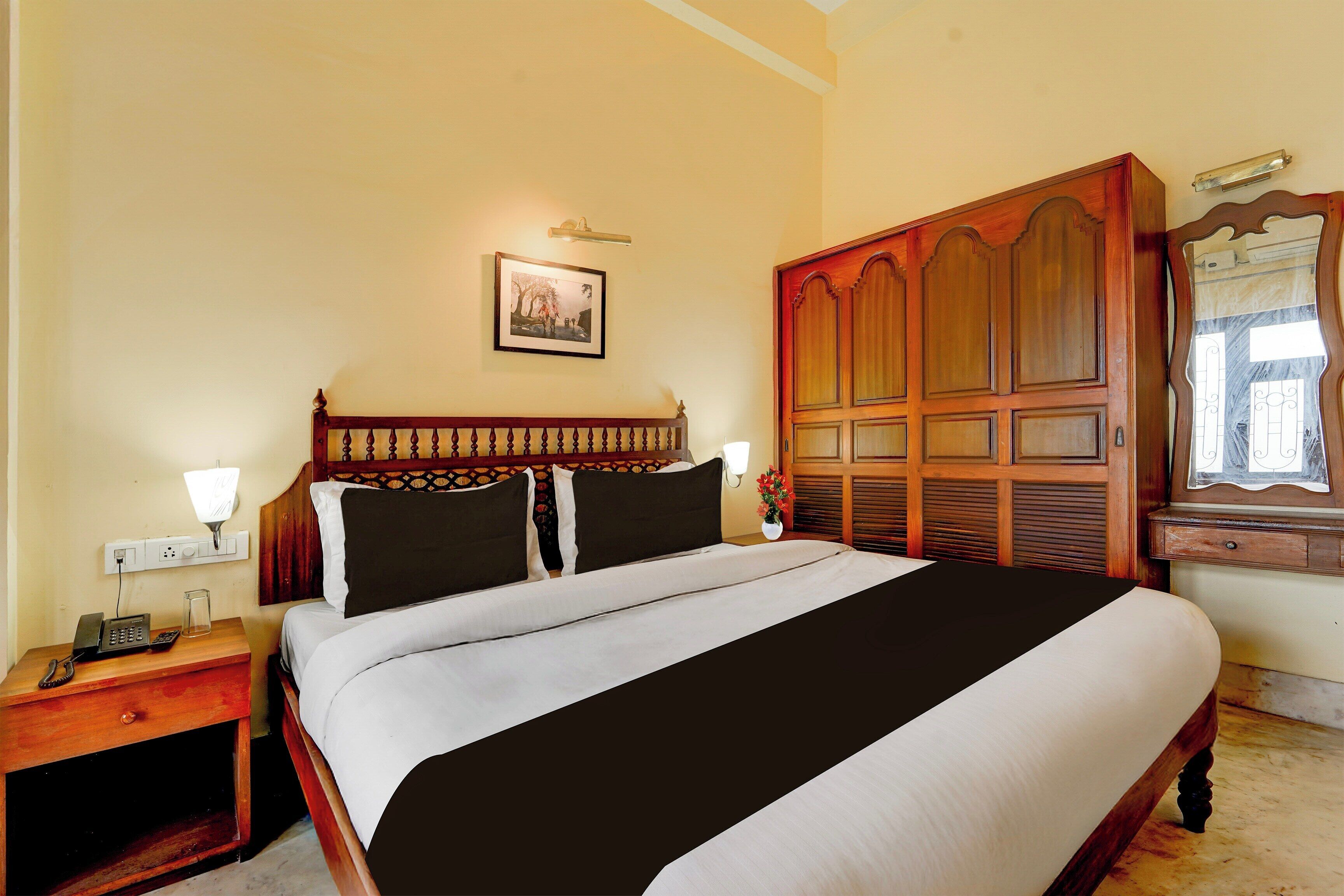 A hotel room with a large bed, a bedside table with a lamp, a telephone, and a mirror.