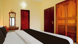 Hotellihuone, jossa on sänky, puinen vaatekaappi, peili ja seinään kiinnitetty valaisin.