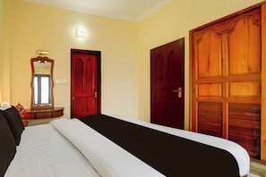 A hotel room with a bed, a wooden wardrobe, a mirror, and a wall-mounted light fixture. - Collection O Kangarappady Formerly (Kanayannur)