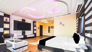 Een moderne hotelkamer met een groot bed, een bureau met stoel, een flatscreen-televisie aan de muur en een plafond met ronde verlichting.