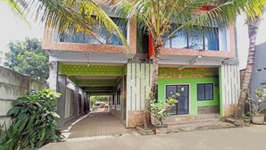 A two-story building with a covered walkway, a green door, and a potted plant. - Penginapan Asri Syariah (Kepanjen)