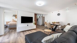 Una sala moderna con una televisión de pantalla plana, un sofá, una mesa de comedor con sillas y un reloj en la pared.